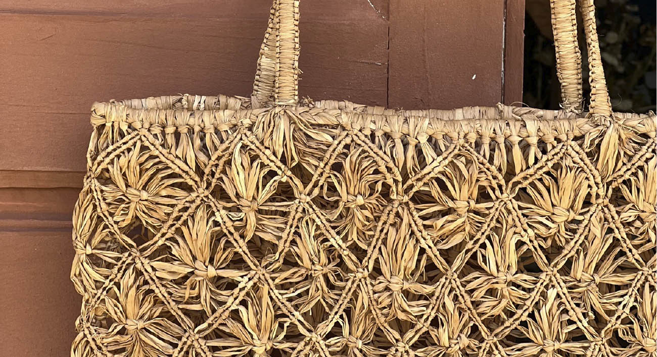 Phot d'un totebag en raphia motif macramé et accroché à une poignée de porte, un totebag macrame couleur thé.