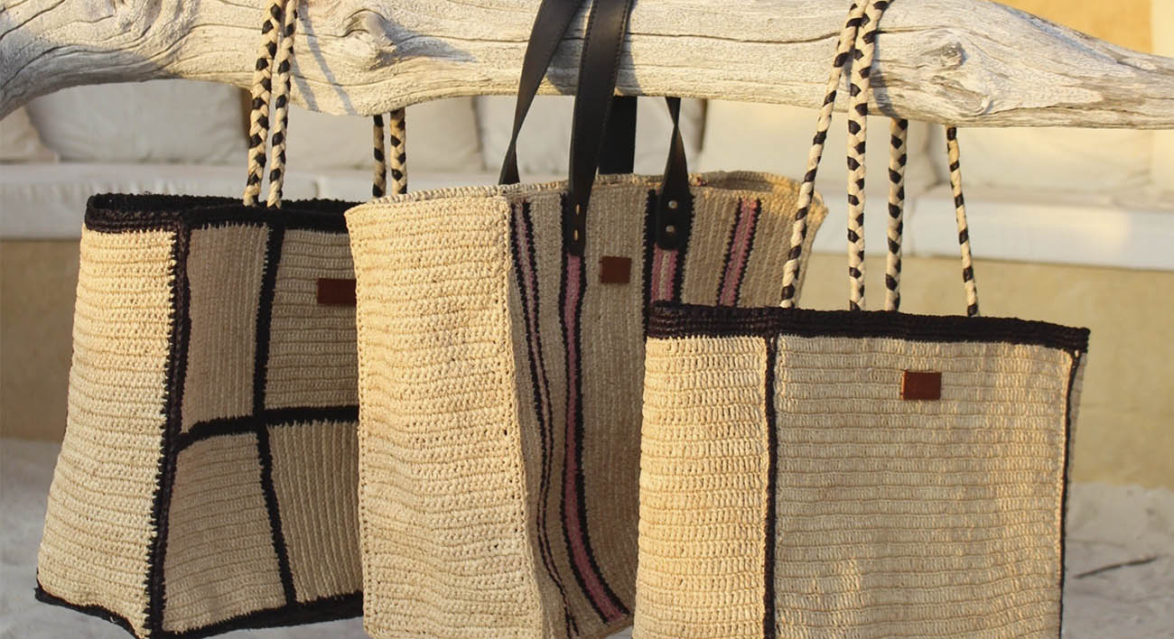 Photo de trois grands cabas en raphia naturel et avec des motifs de rayrues noires, les sacs sont accrochés sur une branche par leur anses solides en raphia tressé ou en cuir véritable.