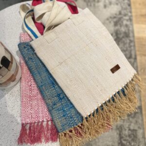 Photo de trois totebags de différentes couleurs, tissage raphia et coton, tissage traditionnel de Madagascar, un blanc, un turquoise et un rose fuschia. Sur la base du totebag, il y a des franges en raphia, les totebags sont posés à plat sur une table. Style bohème.