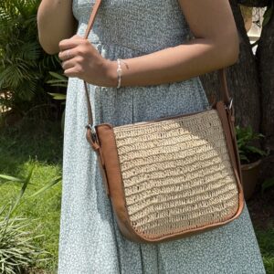 Photo d'un sac à mains de ville, porté avec une bandoulière par une jeune fille, sac en raphia crocheté avec une bande de cuir naturel sur le côté, muni d'une bandoulière amovible en cuir naturelle couleur camel, idéale pour les sorties en ville avec une tenue légère d'été.