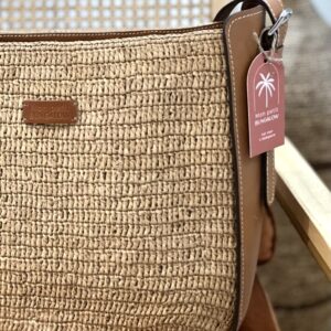 Photo d'un sac à mains de ville, posé sur une chaise, sac en raphia crocheté avec une bande de cuir naturel sur le côté, muni d'une bandoulière amovible en cuir naturelle couleur camel, idéale pour les sorties en ville.