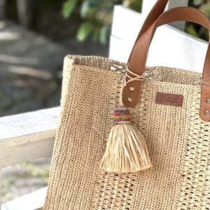 Photo d'un sac moyen cabas LIVIA, en raphia crocheté couleur naturelle, artisanat de madagascar, fait main, porté main par une femme à la plage, ambiance vacances assurée