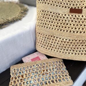 Photo d'un sac en raphia naturel posé à côté d'un canapé, point au crochet motif petits trous, devant le sac est posé une pochette en raphia, fait main, couleur naturelle, doublée en tissu coton imprimé, même point motif petits trous que le sac, deux produits complémentaires.