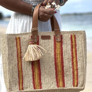 Photo du cabas moyen Maya de Madagascar , porté main par une femme à la plage, artisanat de Madagascar, motif rayures rouges et jaunes.