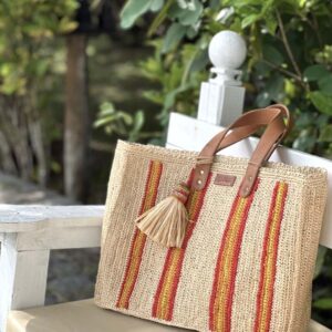 Photo du cabas moyen Maya de Madagascar posé sur un banc, motif rayures rouges et jaunes, en raphia crocheté fait main, artisanat de Madagascar.