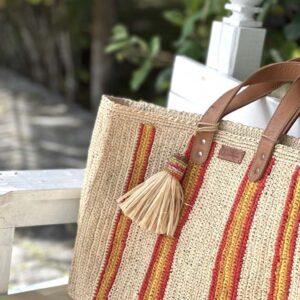 Photo du cabas moyen Maya de Madagascar posé sur un banc, avec des motifs bandes rouges et jaunes.