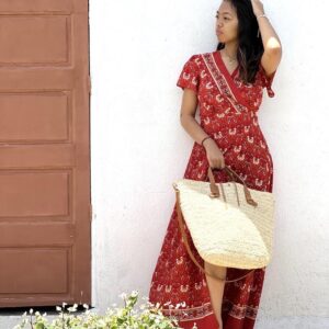 Photo d'une jeune femme appuyée contre un mur avec un grand panier en raphia tressé porté main panier raphia avec une grande bandoulière en cuir naturel couleur camel.